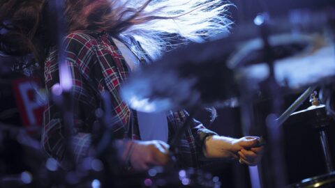 A drummer performs under stage lights. Photo: Nenad Stojković, CC BY 2.0, via Wikimedia Commons.