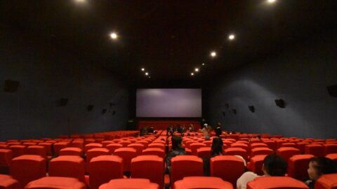 A cinema auditorium with red seats and a large screen