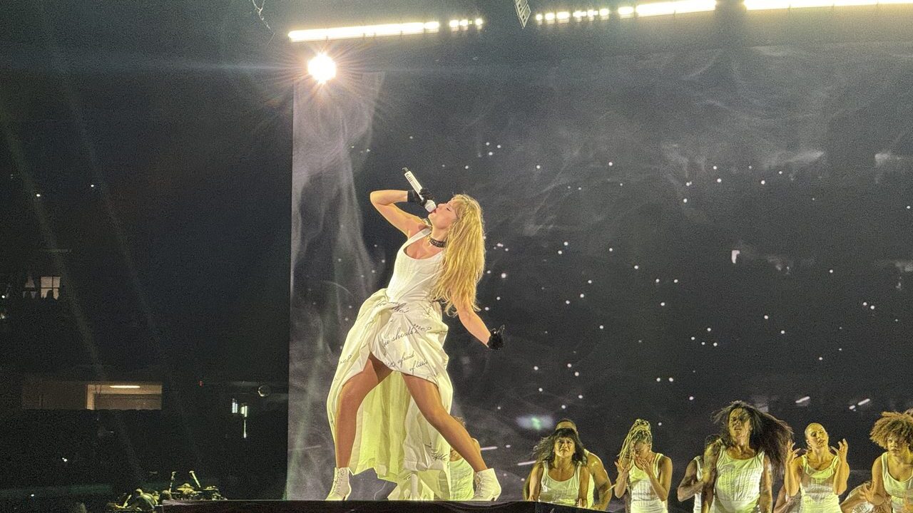 Taylor Swift performing on stage in a white dress during the Eras Tour